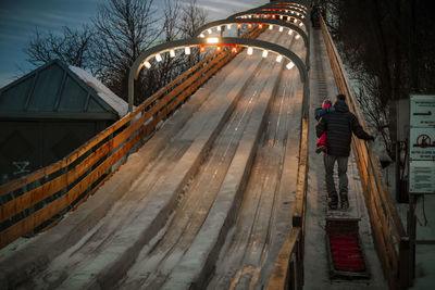 Dad holding his daughter in his arms at icy toboggan at winter dusk