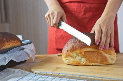Midsection of woman cutting bread in kitchen