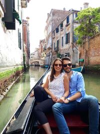 Portrait of smiling couple sitting on boat in canal amidst buildings