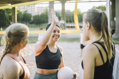 Smiling woman giving high-five to female friend while playing volleyball