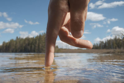 Low section of person legs on lake against sky