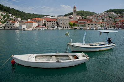 Boats moored in sea by townscape against sky