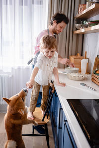 Family fun in the kitchen. cute little boy making whipped cream with his dad and furry friend