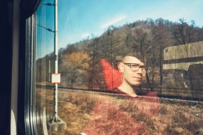 Trees seen through window with reflection of man in train