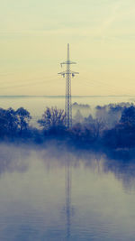 Electricity pylon by river against sky