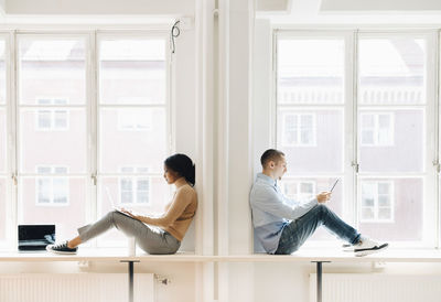 Full length side view of computer programmers working over technologies at desk by window in creative office