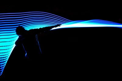 Silhouette person against illuminated blue lights at night