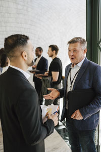 Mature businessman gesturing while explaining male entrepreneur at convention center