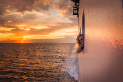 Woman standing by sea against sky during sunset