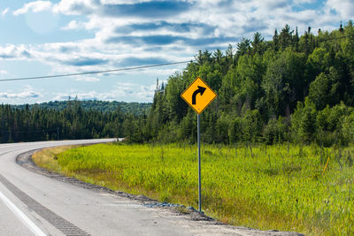 Road sign by trees against sky