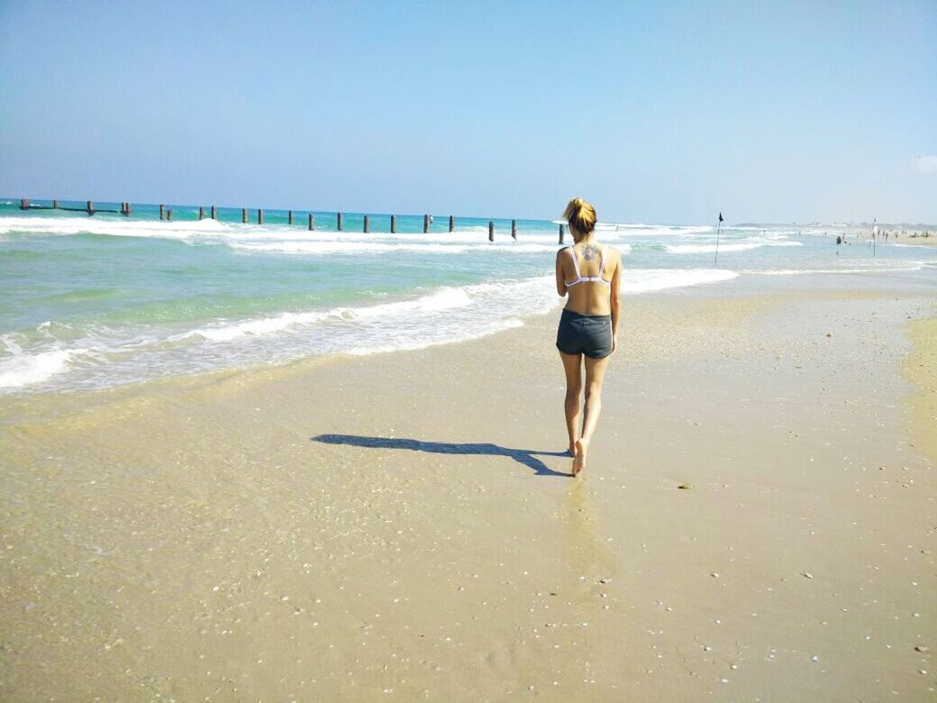 beach, sea, water, shore, sand, horizon over water, full length, lifestyles, clear sky, leisure activity, rear view, casual clothing, walking, vacations, wave, standing, copy space, sky