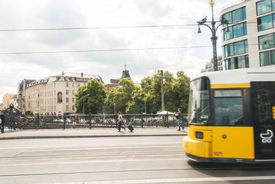 Tramway on railroad track in city against cloudy sky