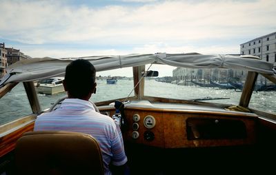 Rear view of man sitting on boat in sea against sky