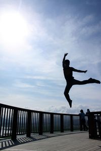 Low angle view of man jumping on railing against sky