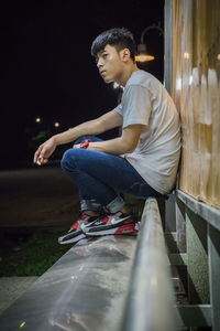 Side view of young man looking away while sitting against wall