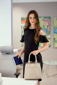 Portrait of businesswoman holding purse and diary in office