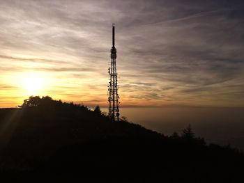 Silhouette electricity pylon on mountain by sea against sky during sunset