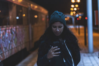 Woman using mobile phone at railroad station in city at night
