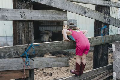 A young girl stands on a fence wearing a leotard and cowgirl boots.