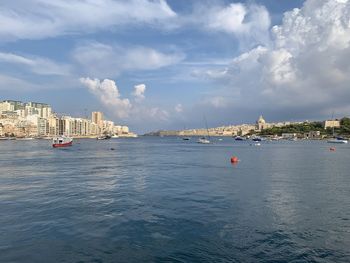 Sailboats in sea by buildings against sky