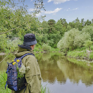 Active male in protective suit with backpack standing near river in a forest. solo traveling