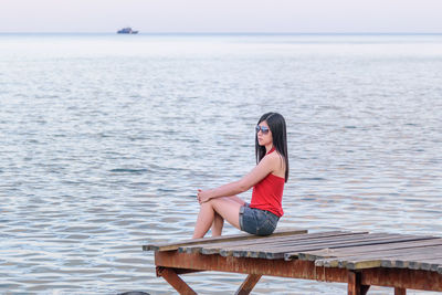 Mid adult woman sitting on pier over sea