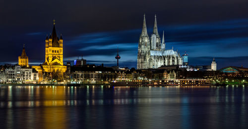 Illuminated buildings and cologne cathedral by rhine river in city at night