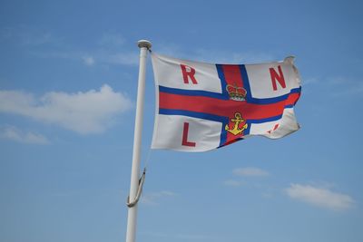Low angle view of rnli flag against blue sky