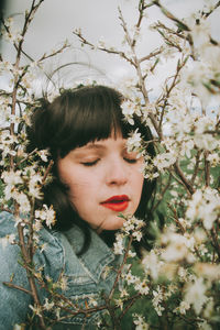 Portrait of young woman with flowers against tree