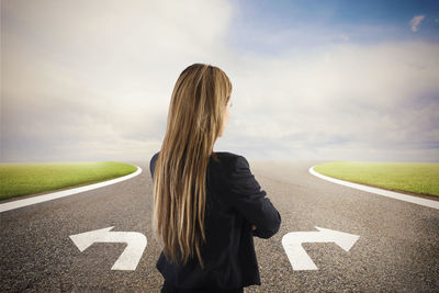 Rear view of woman standing by road against sky