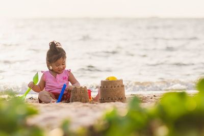Smiling girl sitting by sandcastle on beach