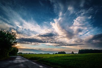 Road amidst agricultural field against sky during sunset