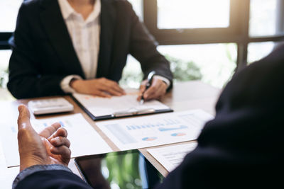 Midsection of colleagues analyzing data on office desk