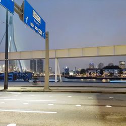 Road sign by illuminated city against clear sky