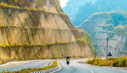 Person riding motorcycle on road by mountain