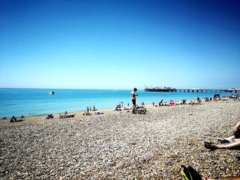 People on beach against clear blue sky