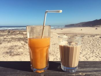 Close-up of orange juice by coffee on table at sandy beach