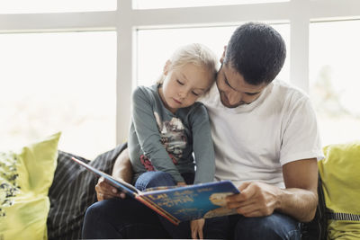 Male teacher and female student reading story book at day care center