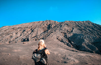 Rear view of woman standing on land against mountain and sky