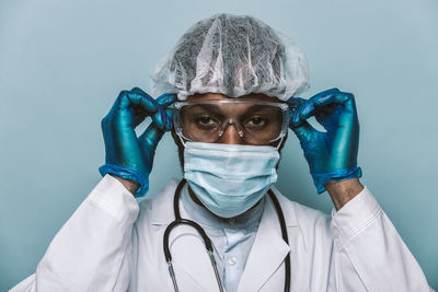 Portrait of doctor wearing mask standing against blue background