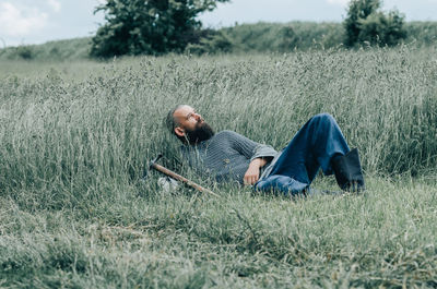 Courageous man with beard resting in grass in field. pensive gaze directed to sky. 