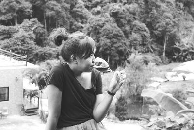 Woman drinking wine in glass while sitting against trees