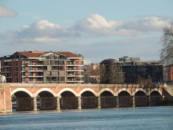 Arch bridge over river by buildings against sky