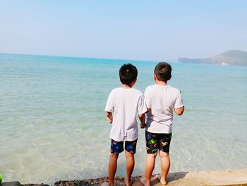 Rear view of boys standing on shore at beach