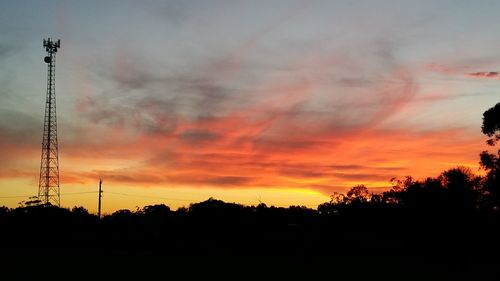 Silhouette trees and electricity pylon against sky during sunset