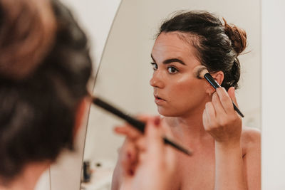 Mirror photo of beautiful young woman putting on makeup