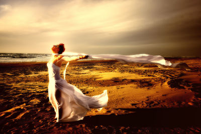 Woman standing on beach against sky during sunset