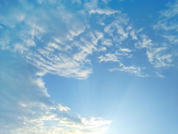 Low angle view of sunlight streaming through clouds