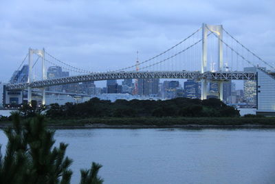 Rainbow bridge in city against cloudy sky at dusk