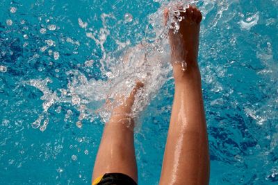 Low section of woman splashing water in swimming pool